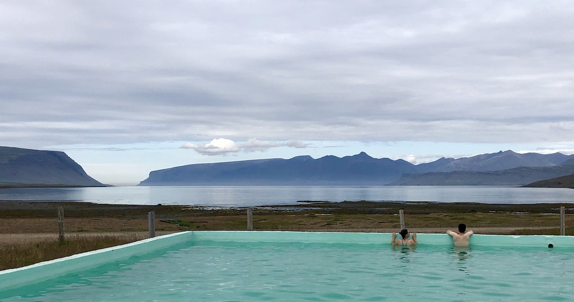 Two people in a hot springs looking at the sea and mountains.