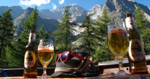 Tour du Mont Blanc Beer Break: Birra Moretti, Tyrolean hat with sunglasses and the mountains of Mont Blanc in the background.