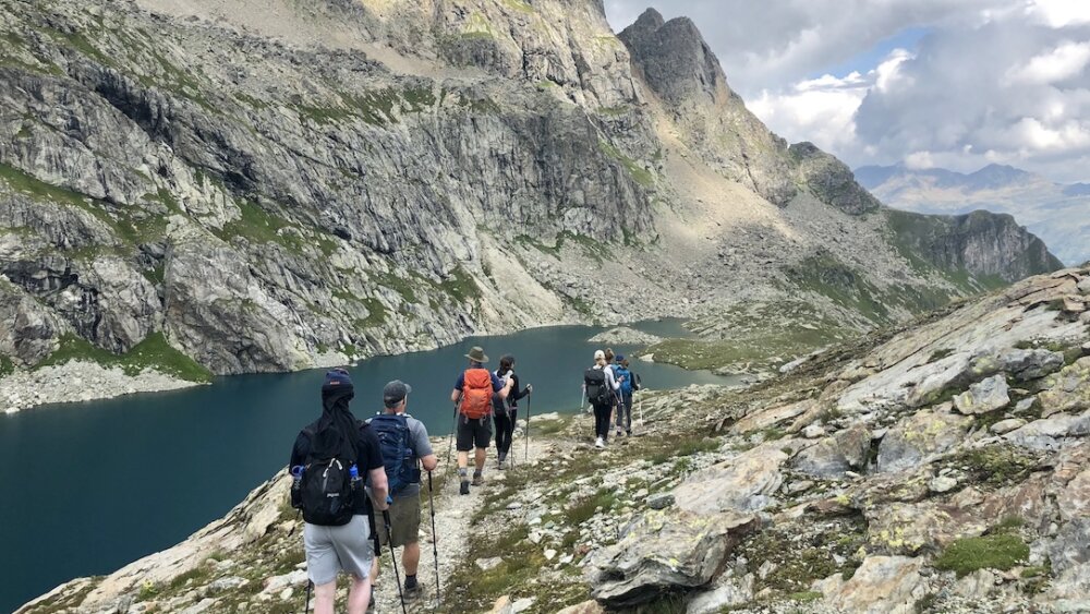 A group of hikers walking a perfect trail next to a high alpine lake.