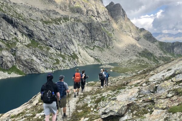 A group of hikers walking a perfect trail next to a high alpine lake.