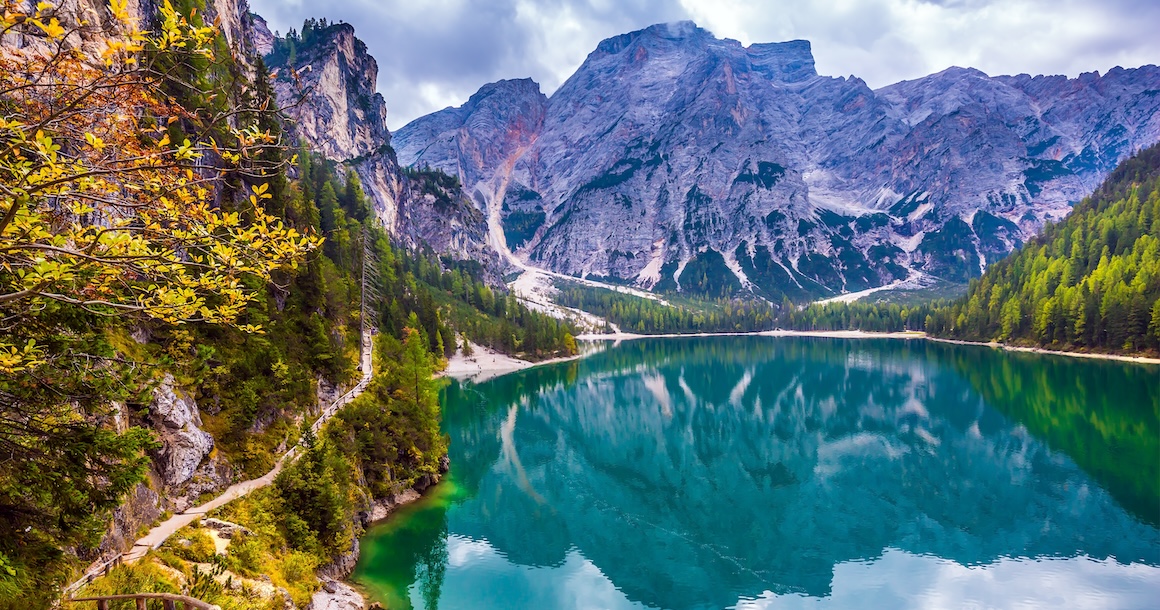 The emerald smooth surface of water reflects the wood and mountains around.