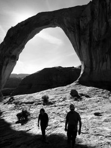 Two hikers walk beneath Corona Arch in Moab, Utah.