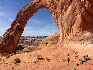A group of hikers looks up at Corona Arch in Moab, Utah.