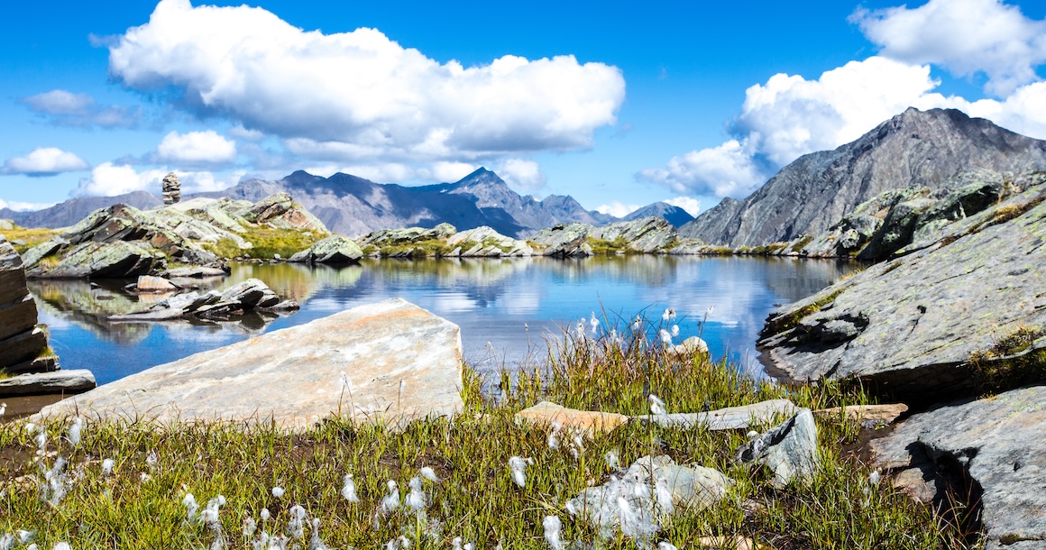 A beautiful lake in the high alpine with rocks in the front and peaks in the far background.